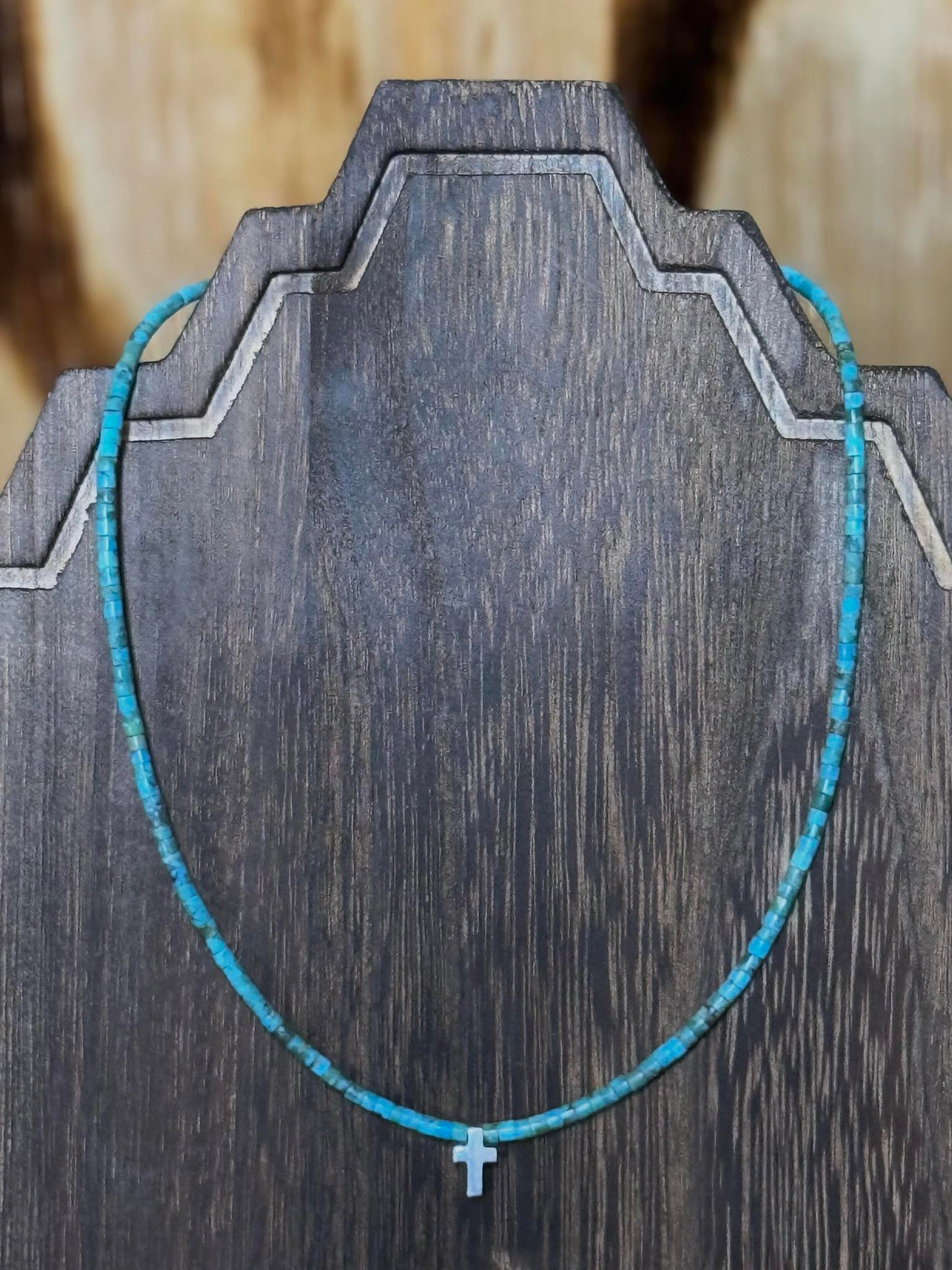 Turquoise rondelle beads with sterling silver cross pendant necklace on wooden display.