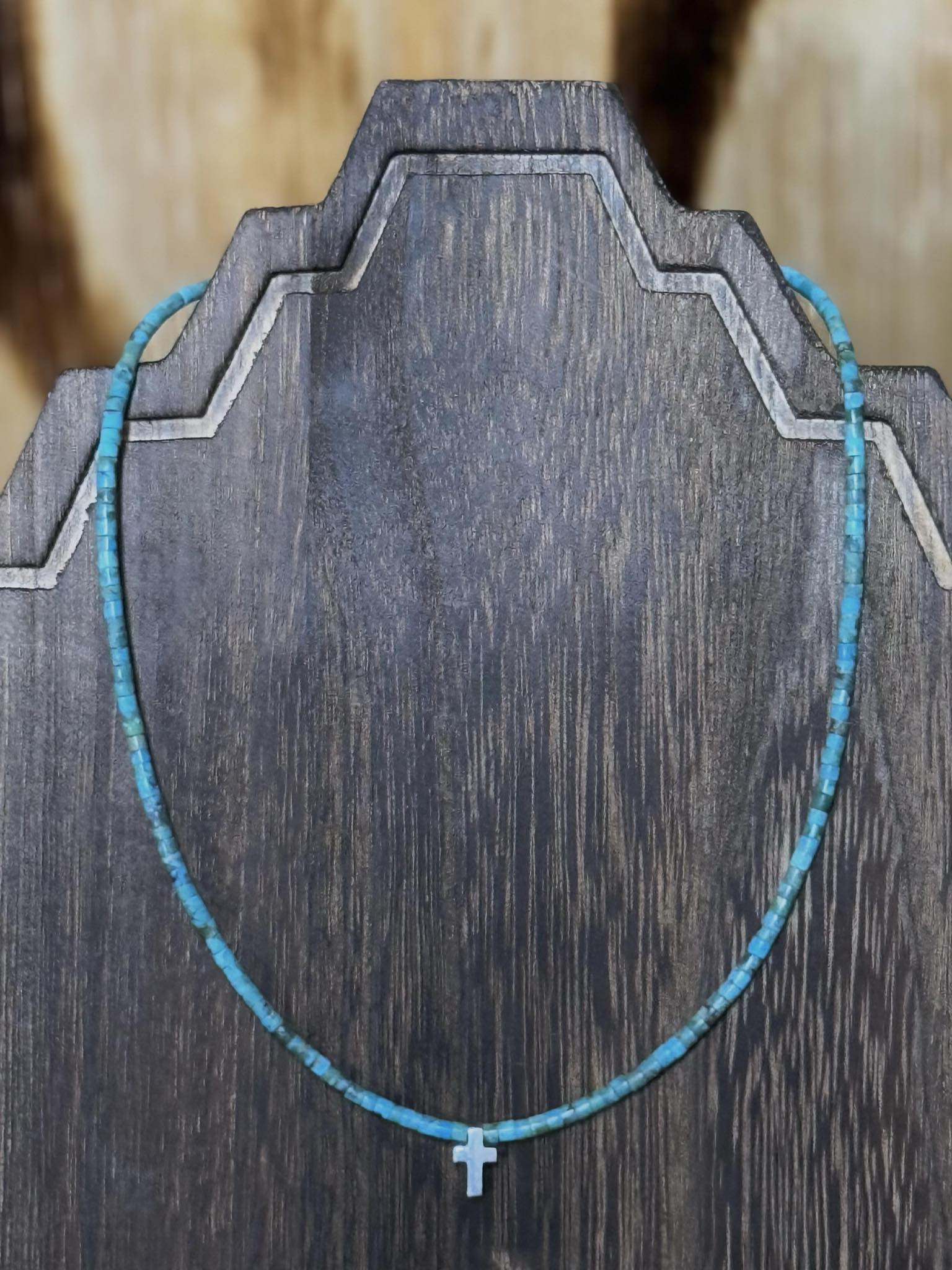 Turquoise rondelle beads with sterling silver cross pendant necklace on wooden display.